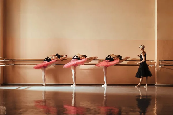 Ballet teacher supervising female ballet dancers during stretching exercises on a barre at dance school. Copy space.