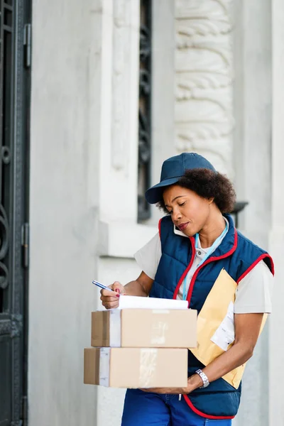 Black Female Courier Taking Notes While Talking Phone Making Delivery — Stockfoto