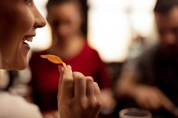 Close up of young woman eating tortilla chips while having fun with her friends in a tavern.