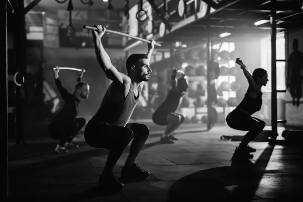 Black and white photo of group of athletes exercising with weight bars on sports training in a gym.