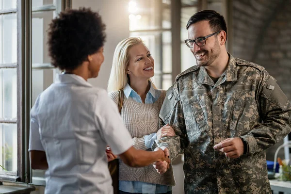 Happy military man shaking hands with female doctor while being with his wife at medical counselling.