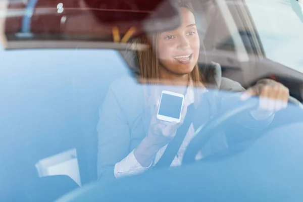 Businesswoman commuting to work by car and talking on mobile phone while driving. The view is through the glass.