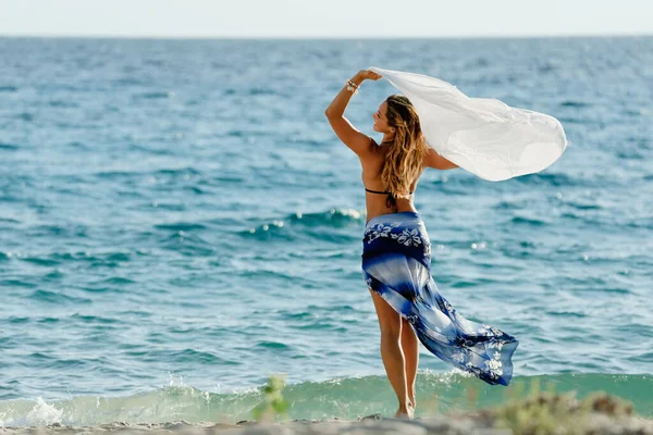 Carefree woman with a scarf having fun in summer day at the beach.