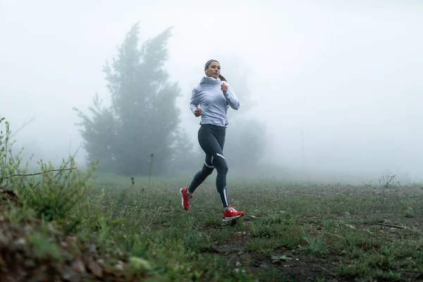 Athletic woman exercising on misty day and running in nature. Copy space.
