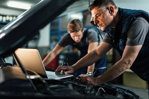 Mid adult mechanic using computer and doing car diagnostic with his coworker in auto repair shop.