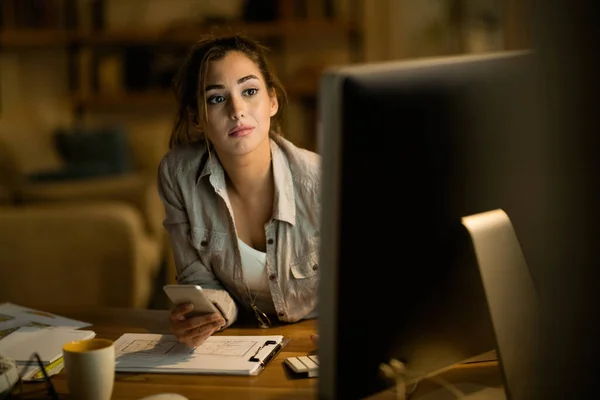 Young woman surfing the net on desktop PC and using smart phone in the evening at home.