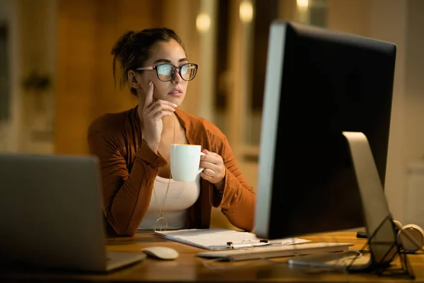 Young Woman Drinking Coffee Thinking While Working Desktop Evening Home — Foto de Stock