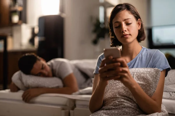 Young Woman Text Messaging Cell Phone While Her Boyfriend Sleeping — Stockfoto