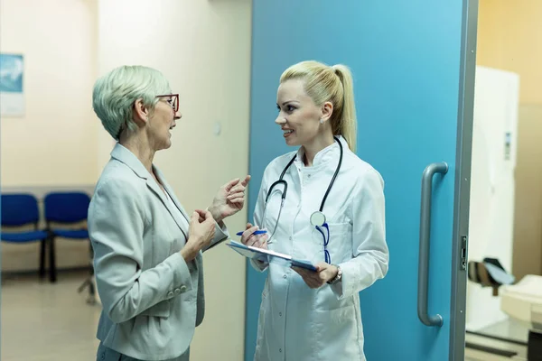 Happy Female Doctor Communicating Senior Patient While Standing Hallway Clinic — Foto de Stock