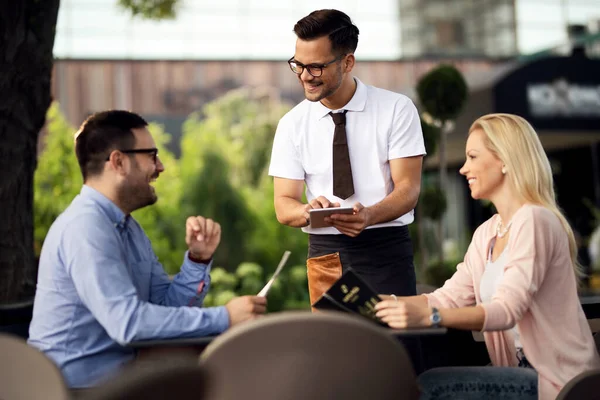 Young Smiling Waiter Using Digital Tablet While Communicating Guest Taking — Stockfoto