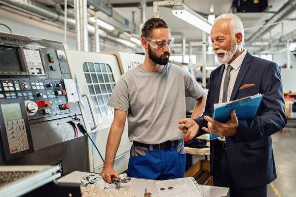 Happy senior company manager talking with young worker while visiting industrial facility.