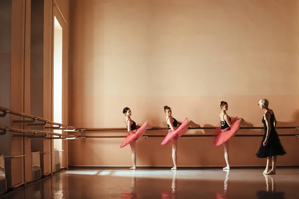 Teenage ballet dancers practicing on a barre while having a class with their instructor at ballet school. Copy space.
