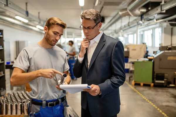 Young steel worker and quality control inspector cooperating while going through paperwork in industrial building. 