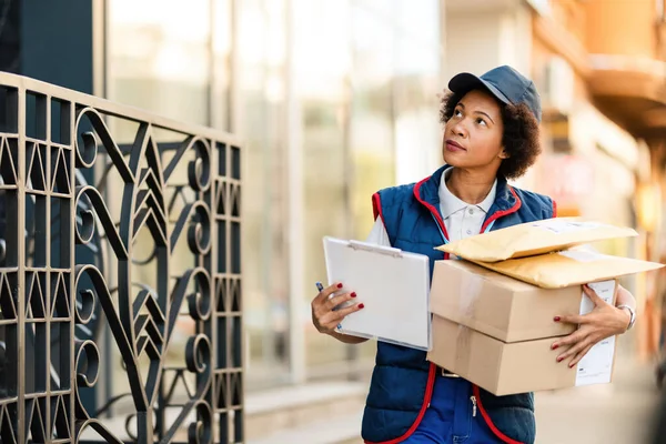 African American female postal worker carrying packages while delivering them in residential district.