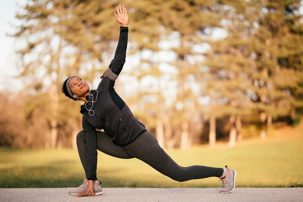 Black female athlete warming up before ports training and doing stretching exercises in the park.