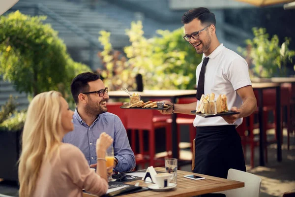 Young Smiling Waiter Serving Couple Bringing Them Food Lunch Time — Fotografie, imagine de stoc