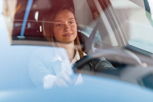 Young businesswoman enjoying going on business travel and driving a car. The view is through the glass. 