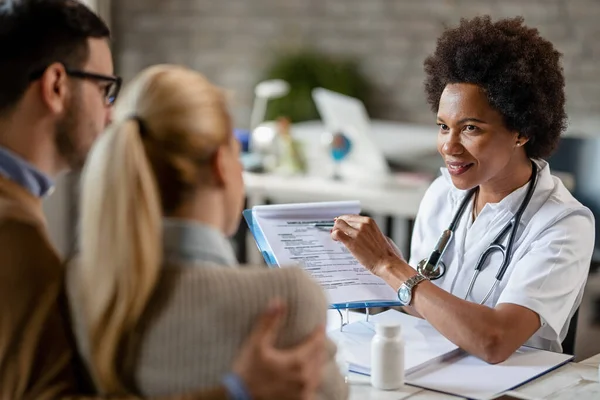 Smiling Black Female Doctor Talking Couple While Analyzing Medical Reports — Fotografia de Stock