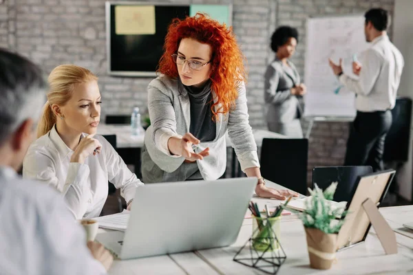 Young serious businesswoman pointing at something on laptop while having a meeting with her colleagues in the office. 