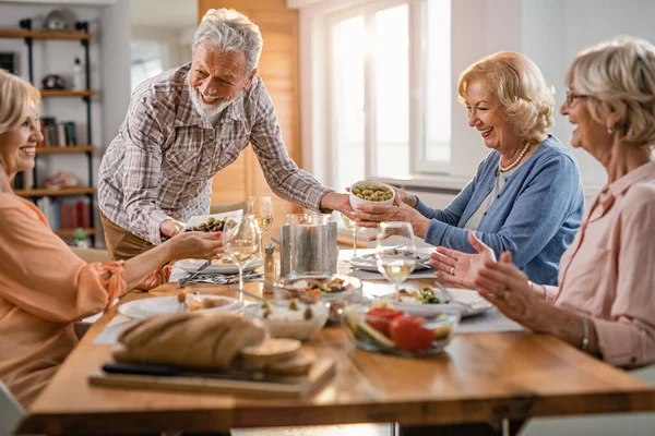 Cheerful Senior Man Serving Food His Female Friends Dining Table — Zdjęcie stockowe