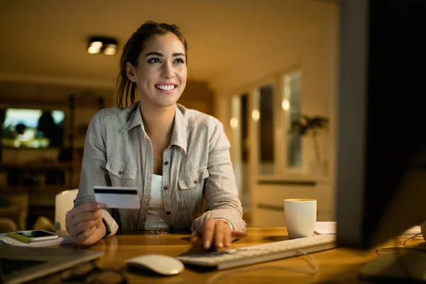 Happy woman using credit card while buying on the internet in the evening at home.