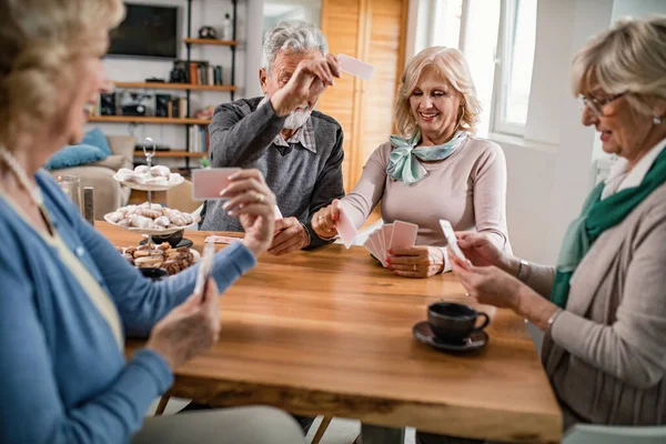 Small group of happy seniors relaxing at home and playing cards together.