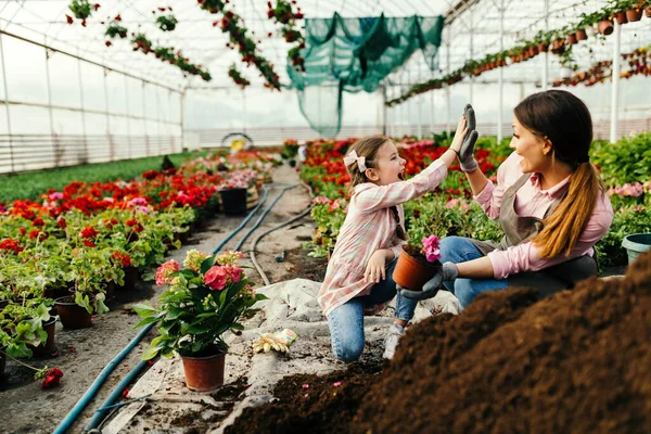 Happy little girl and her mother giving high-five to each other while planting flowers at plant nursery. Focus is on girl.