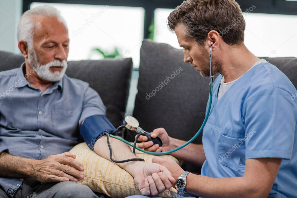 Doctor measuring blood pressure of a senior man while being in a home visit. 