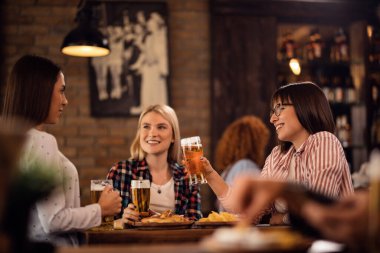 Group of happy young women toasting with beer while gathering in a pub. 
