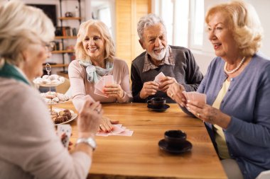 Happy senior couple having fun while playing cards with friends at home. 