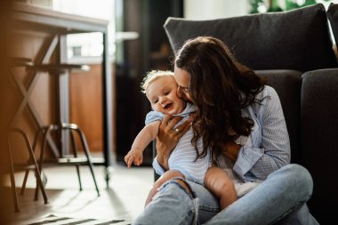 Cute baby boy smiling while his mother is kissing him at home. 