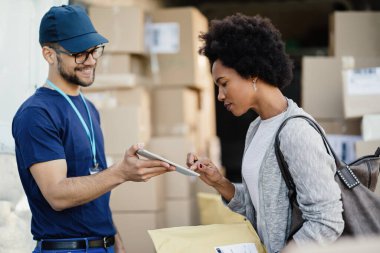 Black woman using digital tablet to sing a delivery form a courier. 
