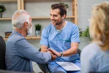 Happy doctor greeting with senior man and shaking hands with him while being in a home visit. 