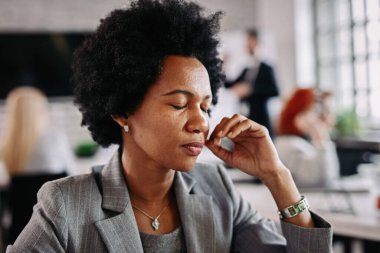 African American entrepreneur feeling exhausted after a busy day at the office. There are people in the background. 