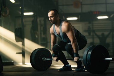 Young sportsman having strength training and lifting barbell in a gym. 