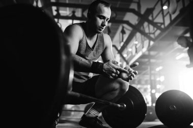 Black and white photo of bodybuilder using talc powder while preparing for weightlifting in a gym. 