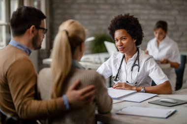Black female doctor having consultations with a couple about their medical insurance at clinic. 