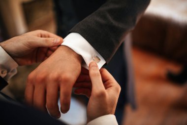 Close up of man helping groom to adjust his suit sleeves on his wedding day. 