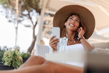 Smiling pensive woman using smart phone and listening music while relaxing in a cafe. 