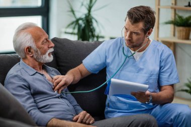 Healthcare worker using stethoscope and listening to heartbeat of his mature patient during a home visit. 
