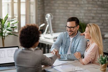 Happy couple handshaking with financial advisor on a meeting in the office. Focus is on man. 