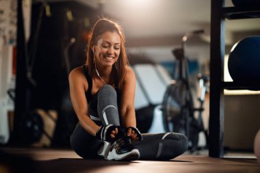 Young happy sportswoman getting ready for a workout and tying shoelace in fitness center. 
