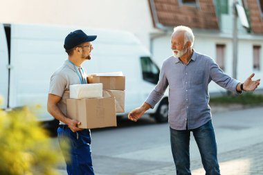 Happy senior man welcoming courier who is delivering him packages at home. 