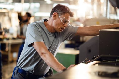 Mid adult industrial engineer operating a CNC machine at production line.