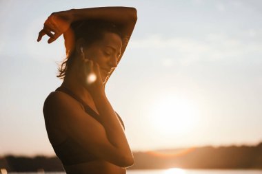 Carefree sportswoman enjoying in early morning sunlight while listening music over earphones in nature. Copy space. 