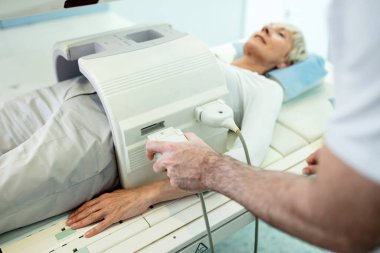 Close up of medical technician preparing female patient for abdomen MRI scan at clinic. 
