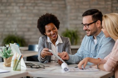 Happy African American financial advisor and a couple using digital tablet during a meeting in the office. 