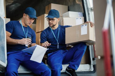 Young couriers going through delivery list while sitting in a van and preparing packages for the shipment. 