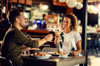 Young happy couple celebrating and toasting with wineglasses while eating in a restaurant. 