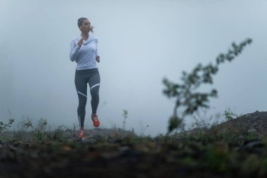 Young motivated runner jogging in nature during cold foggy morning. Copy space. 